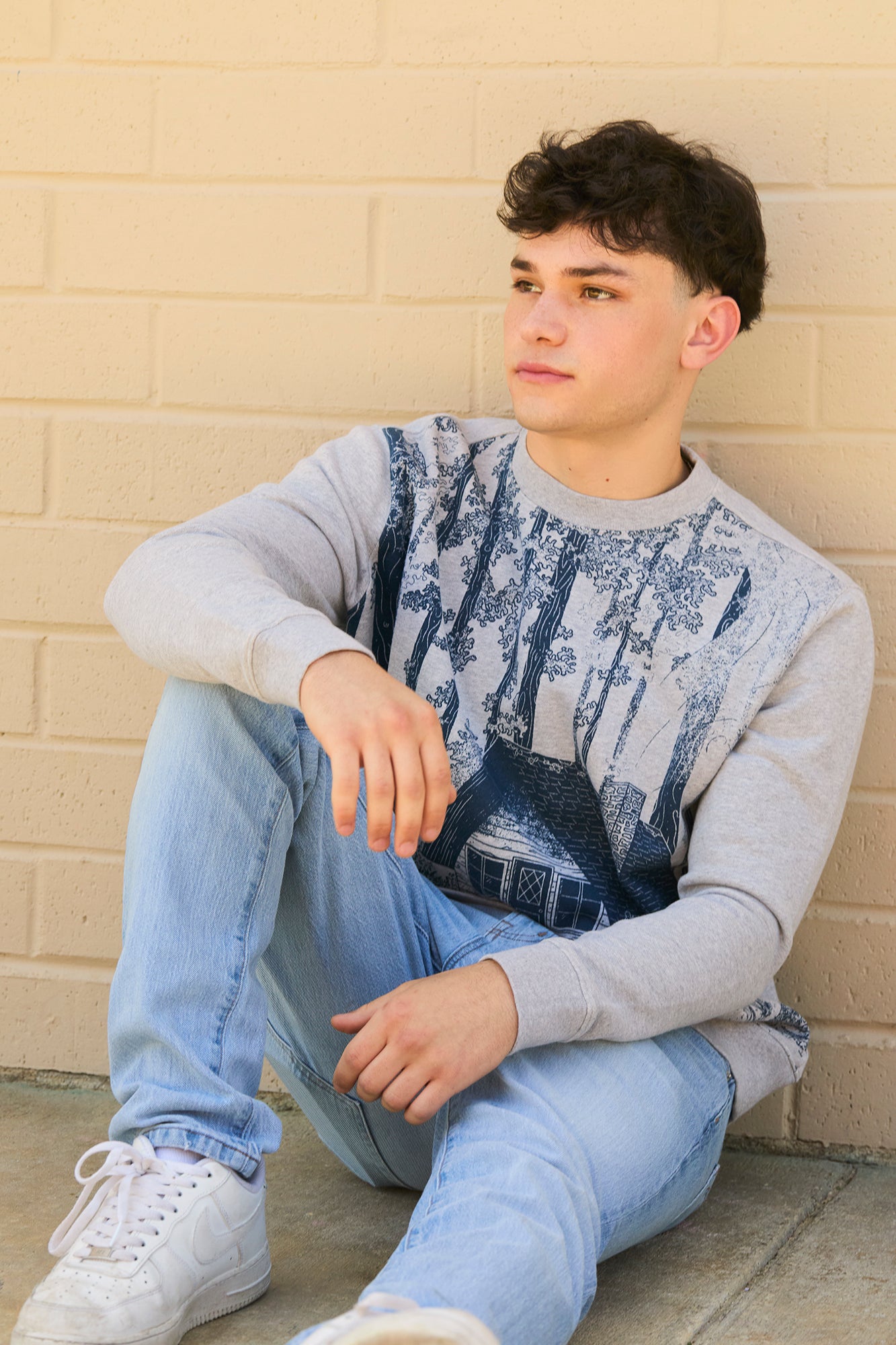 man wearing crewneck decomposition sweatshirt sitting against wall