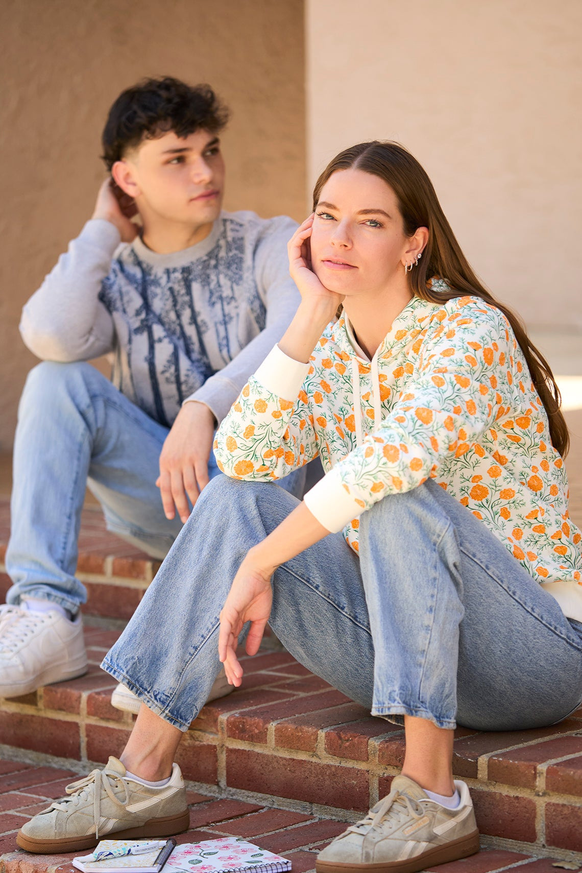 Two people sitting on a set of brick steps with a notebook and pen in front of them.