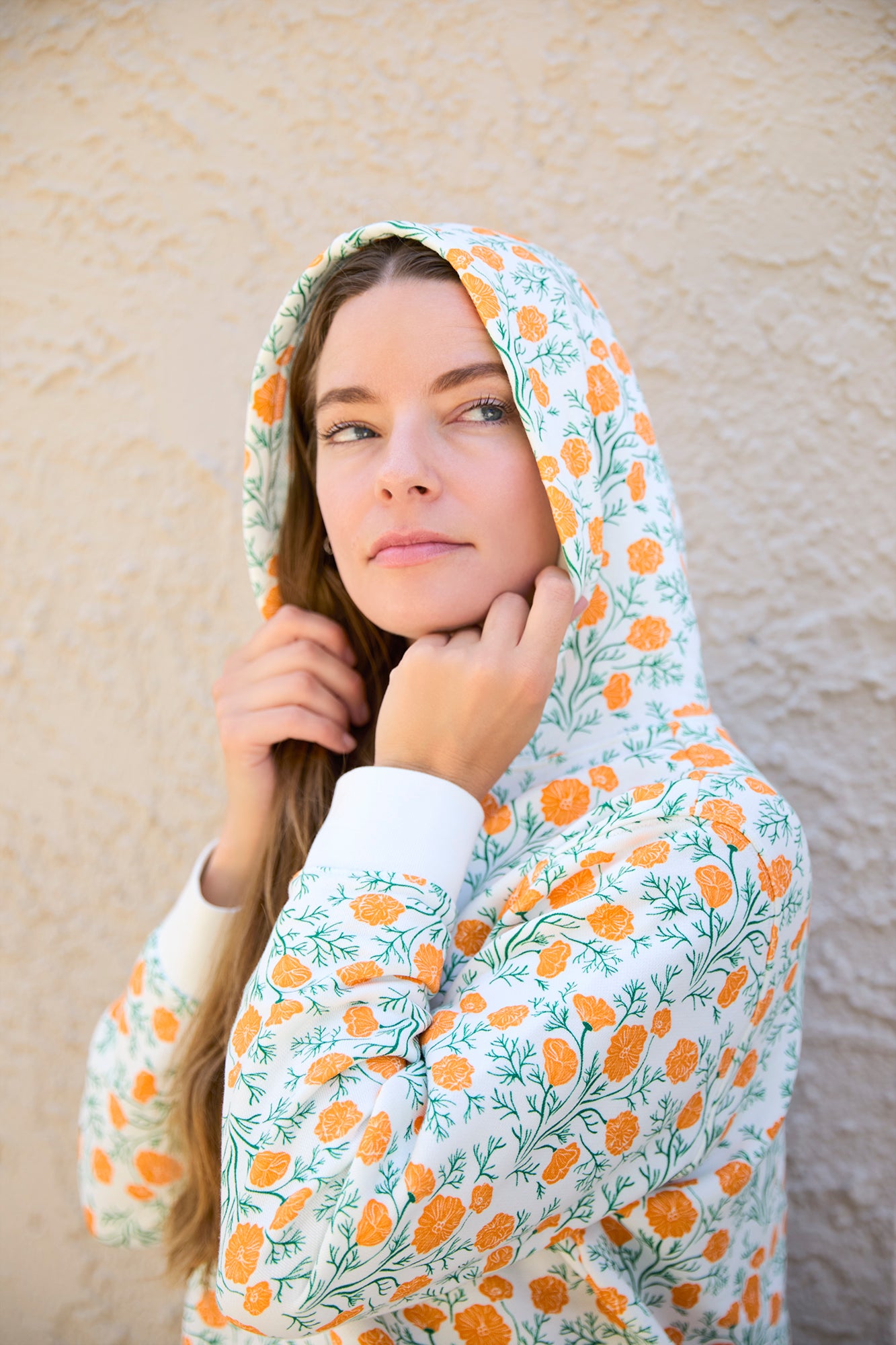A woman wearing a hooded sweatshirt with a floral pattern, featuring orange and green colors on a white background.
