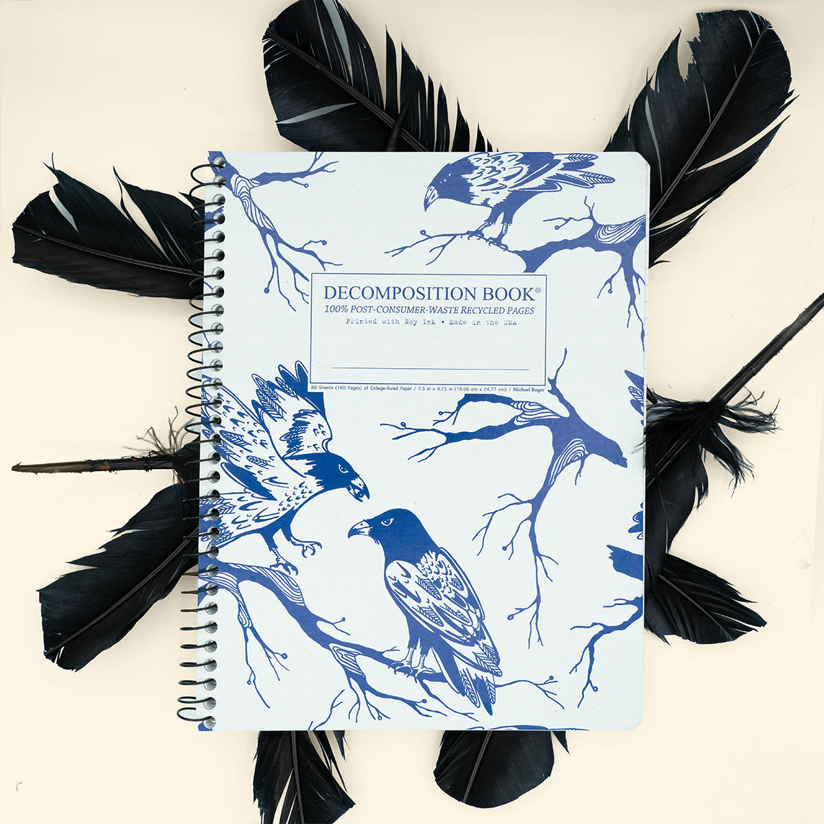 Notebook with bird and branch design on cover, surrounded by black feathers.